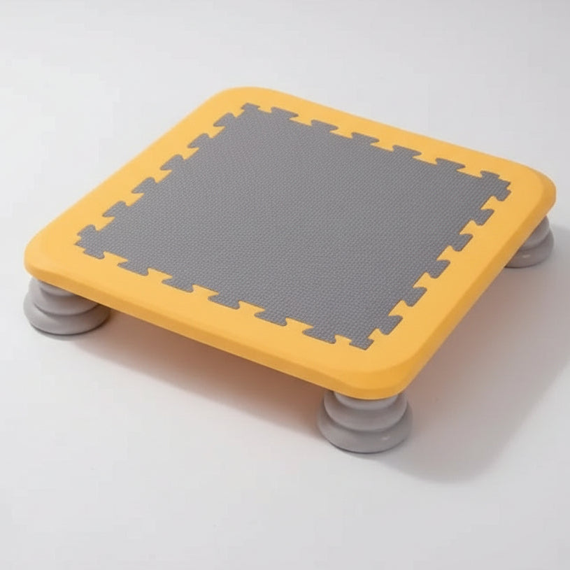 Small square kids’ trampoline with a orange frame, grey jumping surface, and sturdy grey legs designed for sensory play, balance training, and gross motor development.