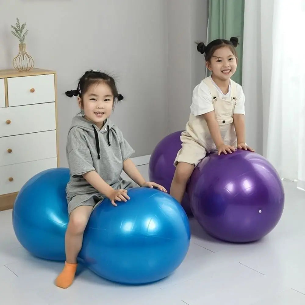 Two children sitting on large blue and purple peanut balls in a room with a white dresser and green curtain.