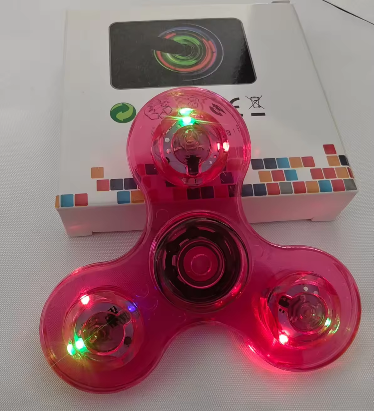 Pink fidget spinner with LED lights in front of its packaging box.