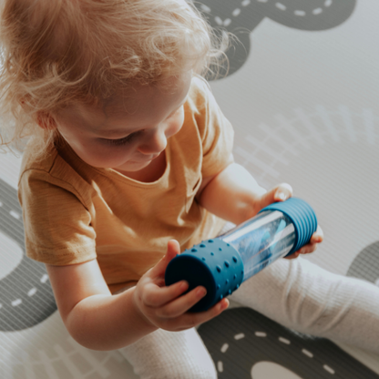 Child holding a blue and clear cylindrical toy on a patterned rug