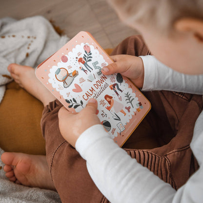 Child holding a book titled '5 Calm Down Activities' on a wooden floor.