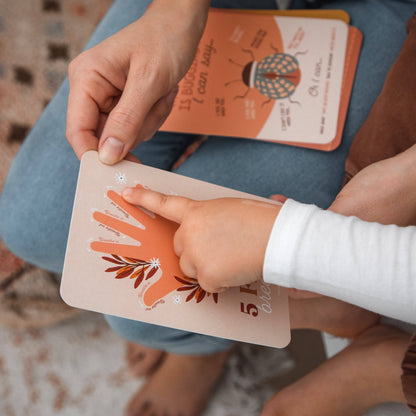 Child's hand holding a small card with a hand design, placed on a larger card with a similar design.