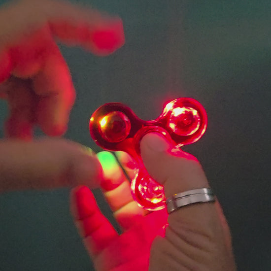 LED fidget spinner with colourful lights spinning in a dark setting.