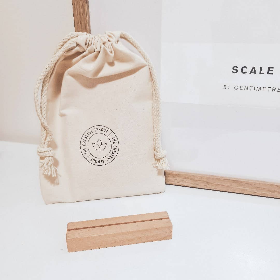 Beige drawstring bag with a logo and a wooden measuring tool on a white surface.